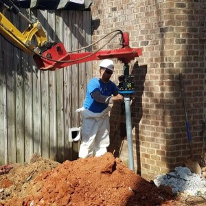 A foundation settlement repair worker installs a helical pier to reinforce a home's foundation.