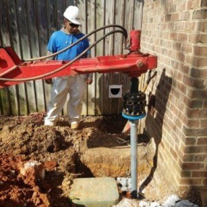 A foundation settlement repair worker installs a helical pier to prevent further damage to a home.