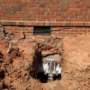 A hole in the ground reveals a home's foundation receiving foundation settlement repair.