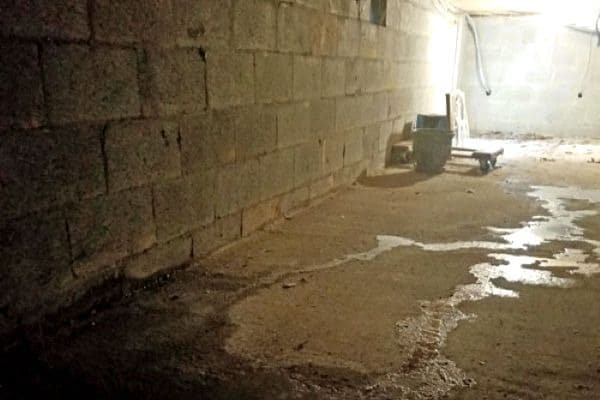 Water leaks in a small space underneath a building that requires crawl space waterproofing.