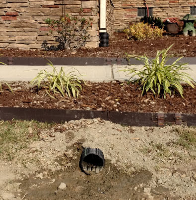 A piece of tubing from a basement waterproofing foundation repair is discreetly installed into a customer's yard.