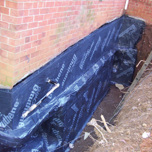 External basement waterproofing material is fixed along a houses foundation.