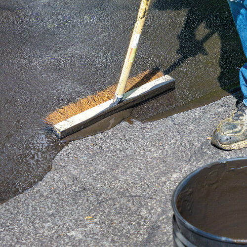 A service worker protects a driveway with concrete and masonry sealant services.